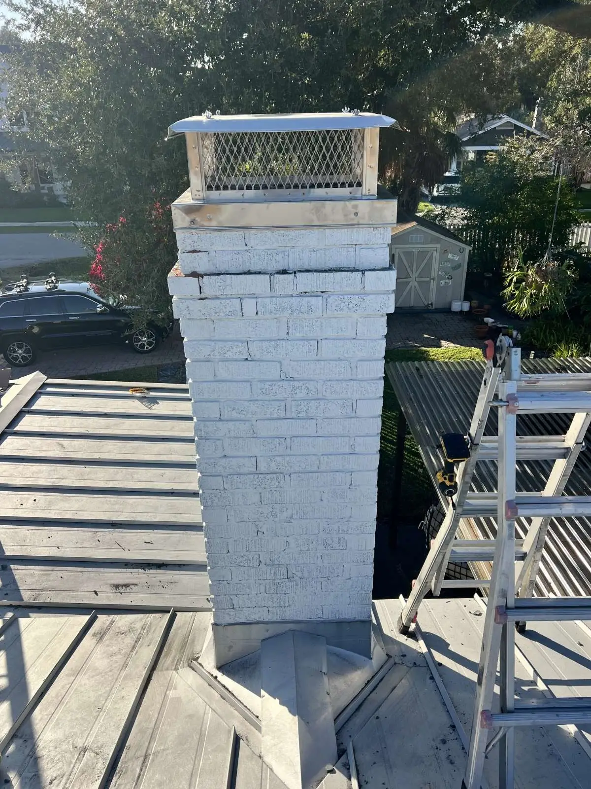 New chimney cap installed on white brick chimney during roof maintenance.