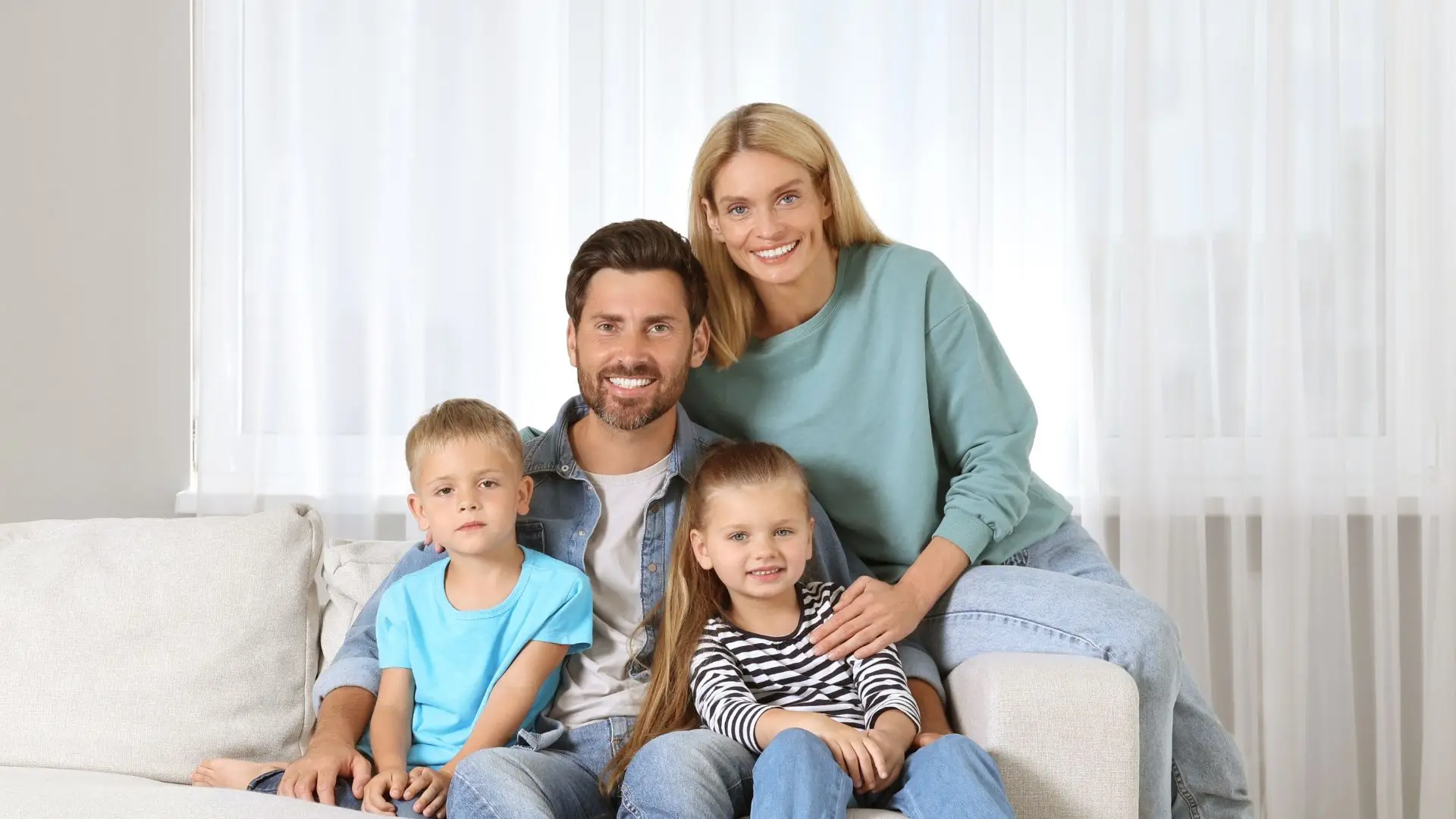 Happy family of four sitting on a couch, enjoying a comfortable indoor environment.