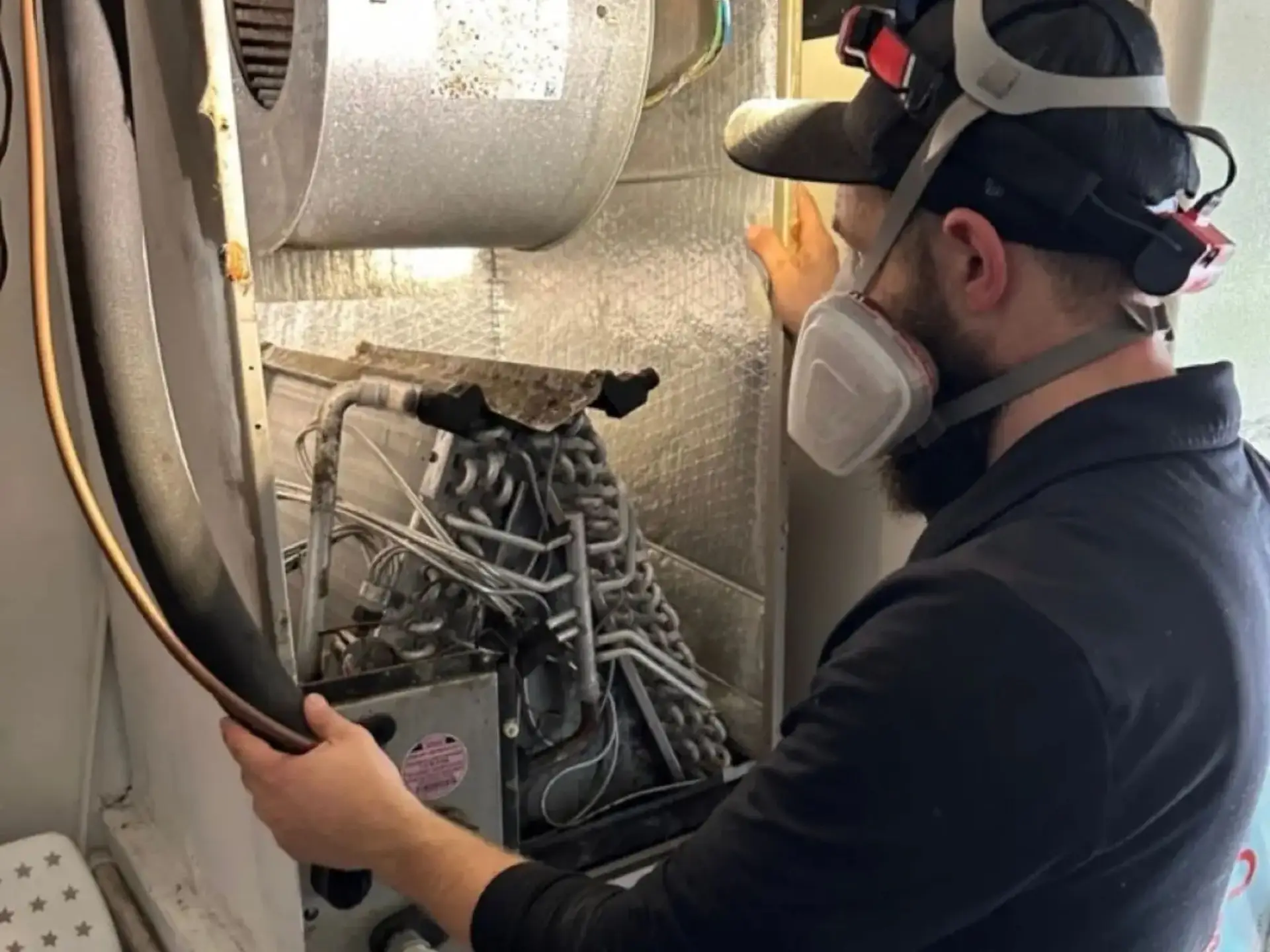 Professional HVAC technician in full PPE and respirator cleaning an evaporator coil. Expert A/C coil maintenance and indoor air quality services by CleanAirPros.