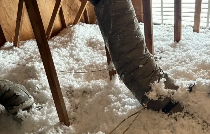 HVAC duct running through attic with blown insulation surrounding the ventilation system.