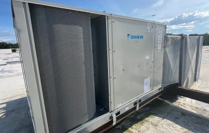 Large silver Daikin commercial rooftop HVAC unit installed on a white membrane roof under a blue sky.