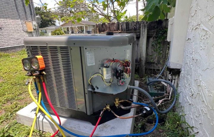 Outdoor HVAC condenser unit with the service panel open and digital manifold gauges connected for testing.