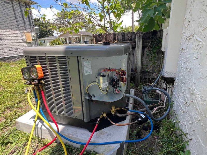 Outdoor HVAC condenser unit with the service panel open and digital manifold gauges connected for testing.