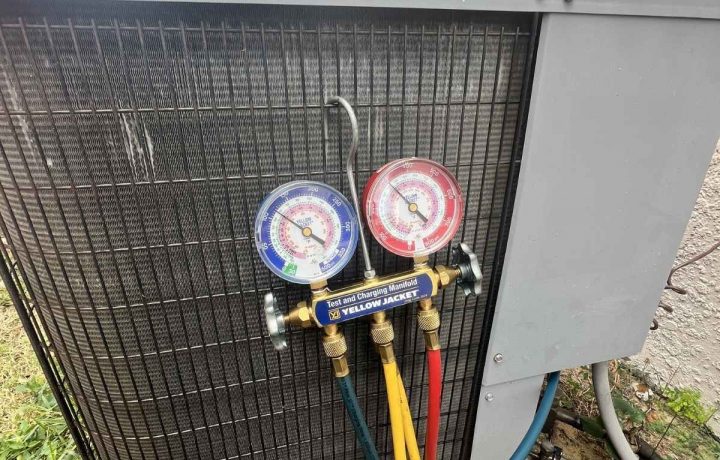 Analog manifold gauges connected to a residential HVAC condenser unit for pressure testing.