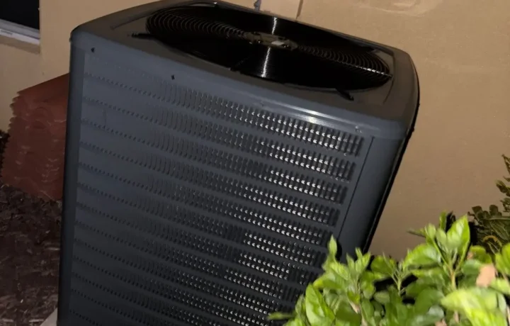 Night-time photo of a modern dark grey HVAC condensing unit installed next to a home.