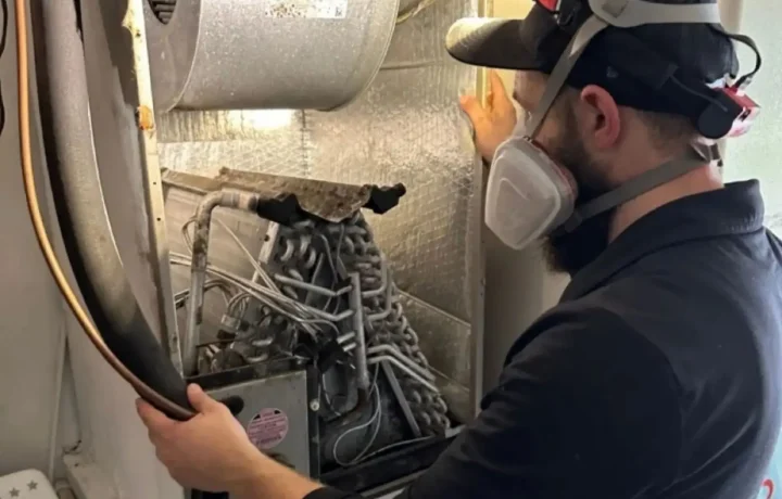 Professional HVAC technician in full PPE and respirator cleaning an evaporator coil. Expert A/C coil maintenance and indoor air quality services by CleanAirPros.