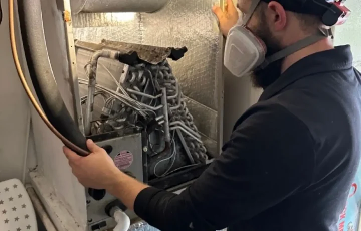 Professional HVAC technician in full PPE and respirator cleaning an evaporator coil. Expert A/C coil maintenance and indoor air quality services by CleanAirPros.