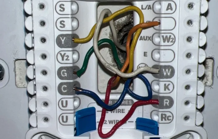 Thermostat wiring installation with visible color-coded connections on the HVAC system's control board.