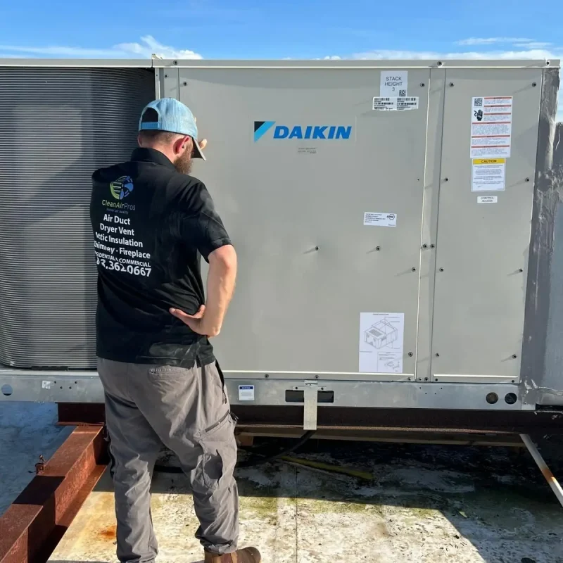 HVAC technician in grey cargo pants standing on a roof inspecting a large Daikin package unit.